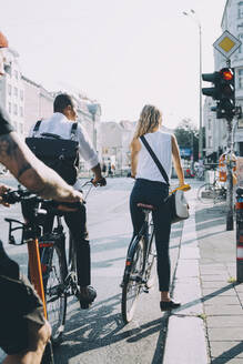 Rückansicht von Geschäftskollegen, die mit dem Fahrrad an einem Signal in der Stadt stehen - MASF17859