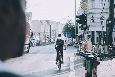 Full length of businessman with backpack riding bicycle on road in city - MASF17862