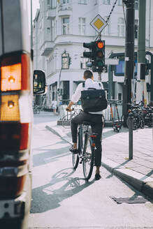 Rückansicht eines männlichen Unternehmers, der auf einer Straße in der Stadt Fahrrad fährt - MASF17864