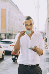 Porträt eines Geschäftsmannes, der in einem Straßencafé in der Stadt Kaffee trinkt - MASF17865
