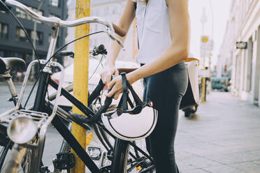 Mittelteil einer Geschäftsfrau, die ihr Fahrrad mit einer Stange auf dem Bürgersteig in der Stadt abschließt - MASF17866