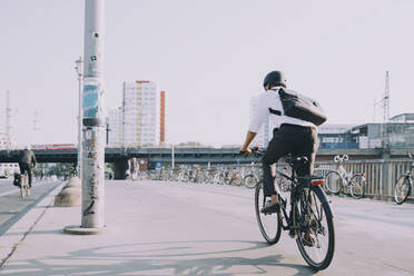 Rear view of businessman riding bicycle on sidewalk against clear sky in city - MASF17870