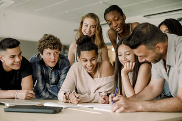 Lächelnde Lehrerin erklärt Teenagern, während sie sich über den Tisch im Klassenzimmer beugt - MASF17882