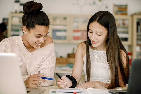 Lächelnde Teenager, die am Tisch im Klassenzimmer sitzen und lernen - MASF17887