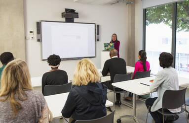 Female community college instructor leading lesson at projection screen in classroom - CAIF25926