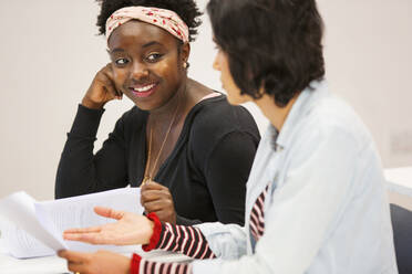 Lächelnde Studentinnen einer Volkshochschule, die sich unterhalten und Papierkram im Klassenzimmer besprechen - CAIF25929