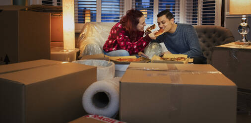 Couple taking a break from moving, eating pizza in living room - CAIF25990