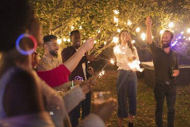 Playful friends with sparklers enjoying garden party - CAIF25991