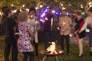 Friends with sparklers around fire pit at garden party - CAIF26013