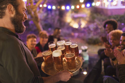 Mann serviert Freunden bei einer Gartenparty ein Tablett mit Bieren - CAIF26029
