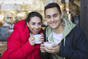 Portrait happy young couple drinking coffee at sidewalk cafe - CAIF26042