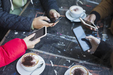 Freunde benutzen Smartphones und trinken Cappuccino am Kaffeetisch - CAIF26044