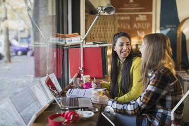 Lächelnde Studentinnen studieren am Fenster eines Cafés - CAIF26046