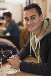 Porträt eines selbstbewussten jungen Mannes, der ein Smartphone in einem Café benutzt - CAIF26052