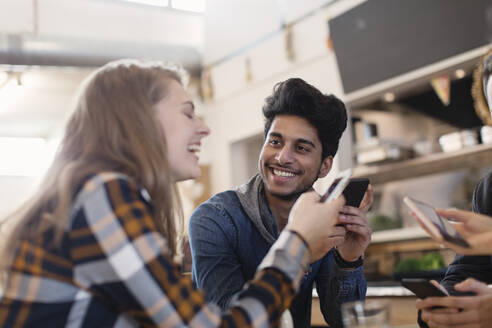 Glückliche junge Erwachsene, die im Café ihr Smartphone benutzen - CAIF26053