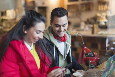 Junges Paar benutzt Smartphone und Laptop in einem Cafe - CAIF26056
