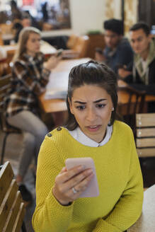 Besorgte junge Frau benutzt ihr Smartphone in einem Café - CAIF26057