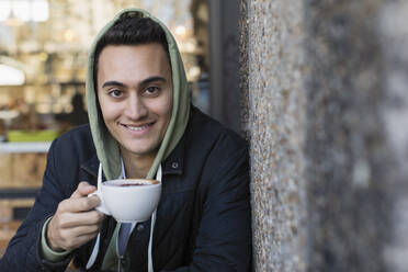 Portrait smiling, confident young man drinking coffee at sidewalk cafe - CAIF26071