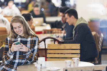 Lächelnde junge Frau mit Smartphone in einem Café - CAIF26073