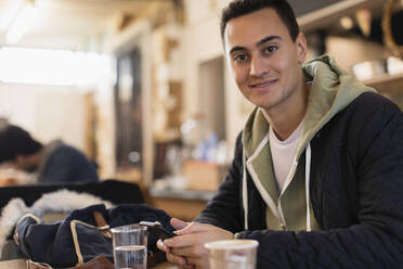 Porträt selbstbewusster junger männlicher Student, der ein Smartphone in einem Café benutzt - CAIF26081