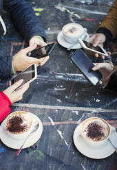 College-Studenten benutzen Smartphones und trinken Cappuccino am Cafétisch - CAIF26084