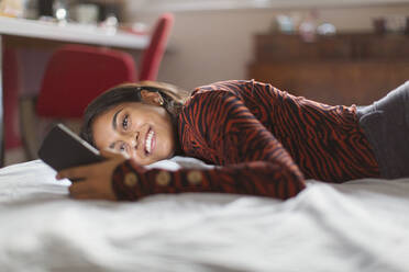 Lächelndes Teenager-Mädchen mit Smartphone auf dem Bett - CAIF26106