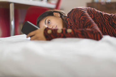 Konzentriertes Teenager-Mädchen mit Smartphone auf dem Bett liegend - CAIF26111
