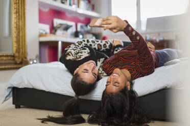 Glückliche Teenager-Mädchen, die ein Selfie auf dem Kopf stehend auf dem Bett machen - CAIF26112