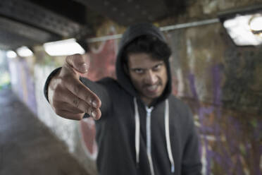 Portrait menacing young man gesturing finger gun in urban tunnel - CAIF26121