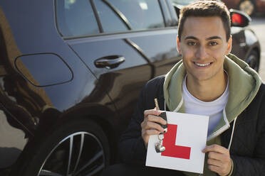 Portrait confident, happy young man holding learners permit by car - CAIF26125