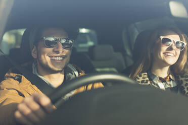 Happy young couple wearing sunglasses in car - CAIF26134
