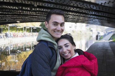 Portrait happy young couple hugging along canal - CAIF26142