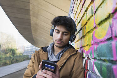 Junger Mann mit Kopfhörern, der auf einem städtischen Bürgersteig Musik hört - CAIF26156