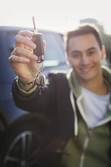 Porträt eines glücklichen jungen Mannes, der neue Autoschlüssel mit einem Schlüsselanhänger in Herzform hält - CAIF26161