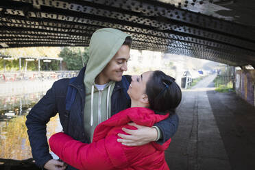 Happy, affectionate young couple hugging under urban bridge - CAIF26164