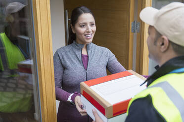 Lächelnde Frau, die ein Paket vom Zusteller an der Haustür erhält - CAIF26169