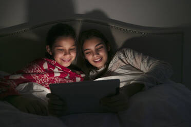 Girls watching movie on digital tablet in dark bedroom - CAIF26170