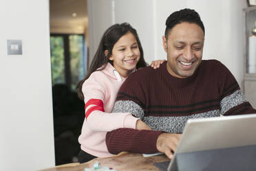 Lächelnder Vater und Tochter benutzen ein digitales Tablet am Tisch - CAIF26176