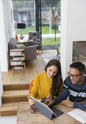 Couple paying bills at digital tablet at dining room table - CAIF26180