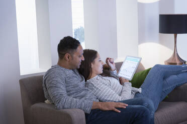 Couple relaxing, using digital tablet on living room sofa - CAIF26187