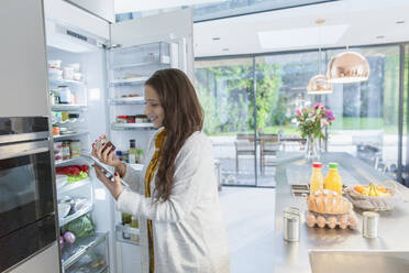 Frau mit digitalem Tablet am Kühlschrank in der Küche - CAIF26188