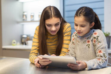 Sisters using digital tablet in kitchen - CAIF26193