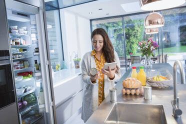 Woman with digital tablet checking food labels in kitchen - CAIF26199