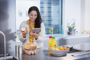Frau mit digitalem Tablet zur Überprüfung von Lebensmitteletiketten in der Küche - CAIF26200