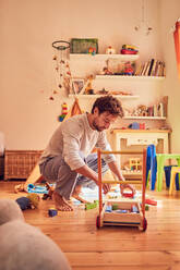 Vater hebt Spielzeug im Kinderzimmer auf - CAIF26232