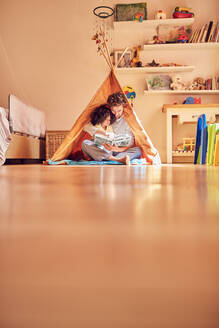 Vater und Tochter lesen ein Buch im Tipi - CAIF26234