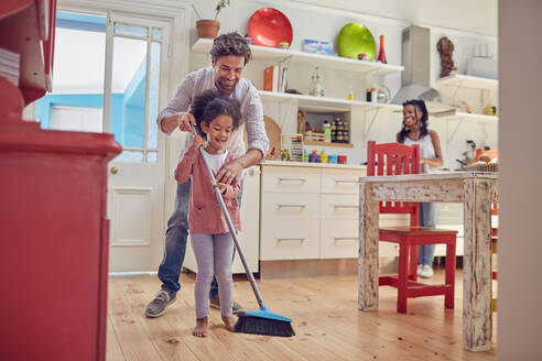 Vater und Tochter kehren den Küchenboden mit einem Besen - CAIF26236