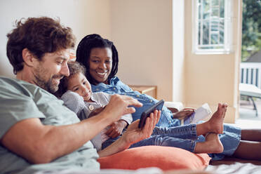 Schwangere junge Familie, die auf dem Sofa ein Smartphone und ein digitales Tablet benutzt - CAIF26245