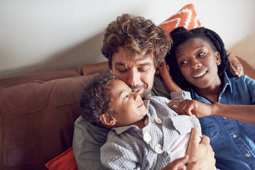 Liebevolle junge Familie kuschelnd auf dem Sofa - CAIF26256