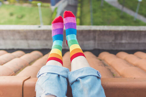 Crop-Ansicht einer Frau, die auf einem Dach sitzt und bunt gestreifte Socken trägt - FVSF00047